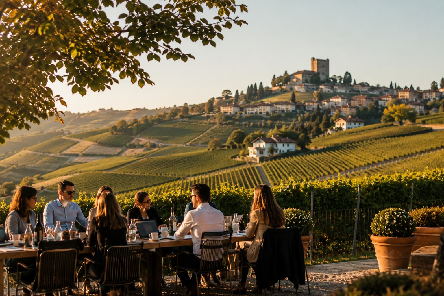 An international team working together at a long outdoor table set among the vineyards of the Langhe, with a hilltop village in the distance — a private corporate retreat in Piedmont