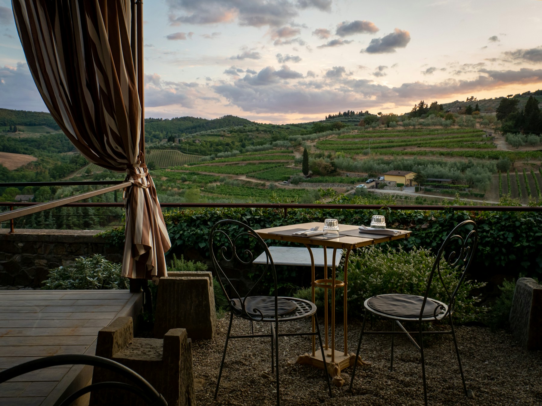A terrace table overlooking vineyards and olive groves in the Italian countryside at dusk