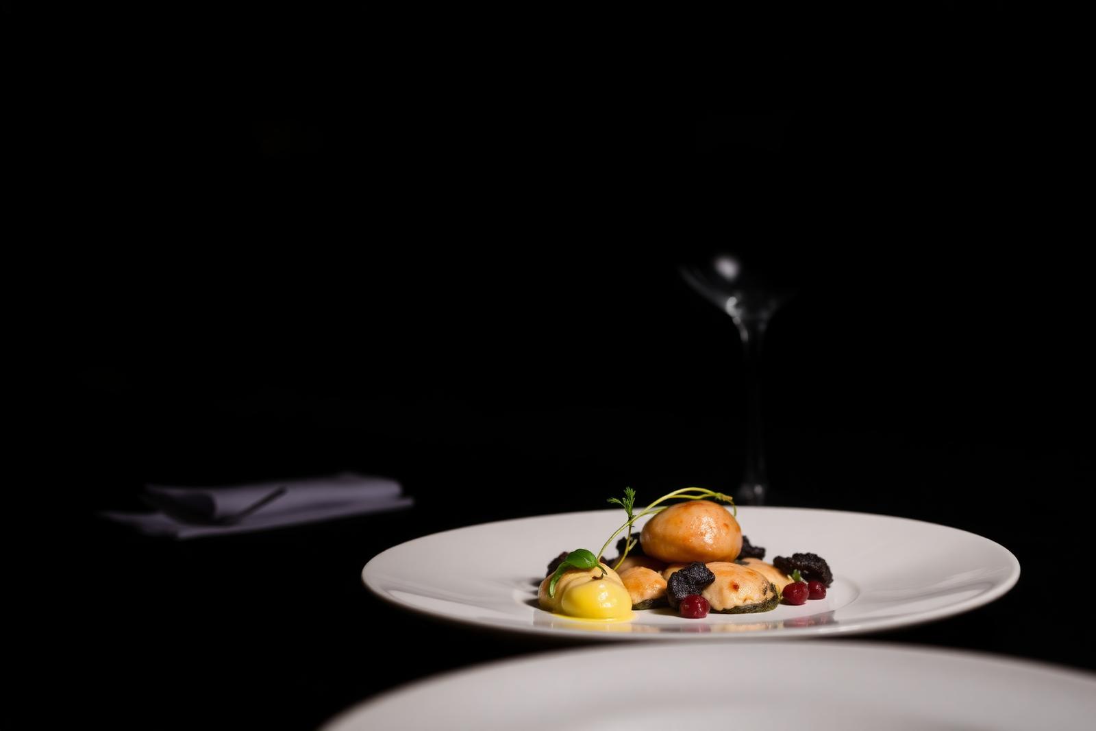 Michelin-star fine dining plate at a Milan restaurant, minimalist plating against a moody dark background