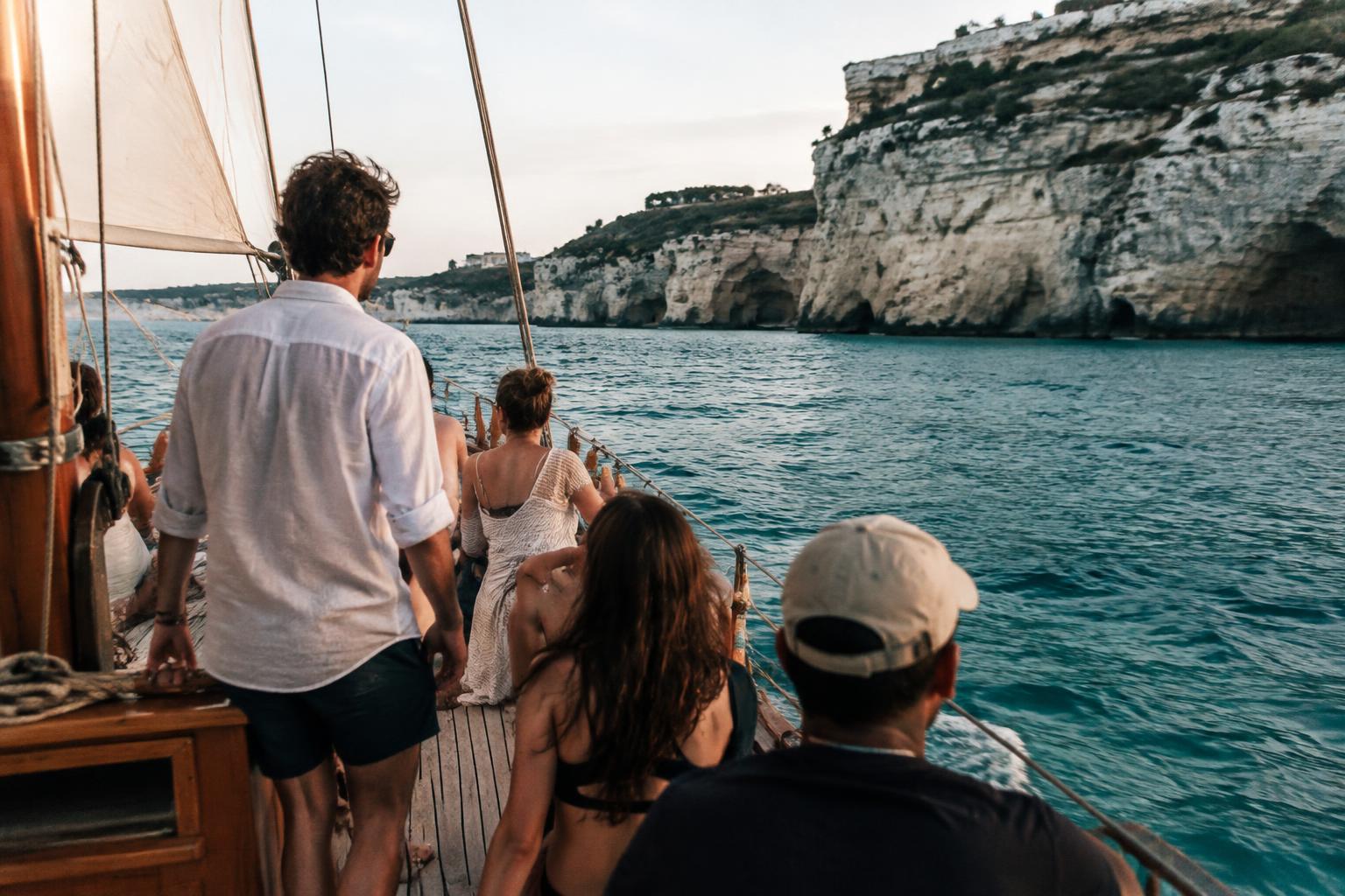 A group on the deck of a wooden sailing boat passing white limestone cliffs on turquoise water